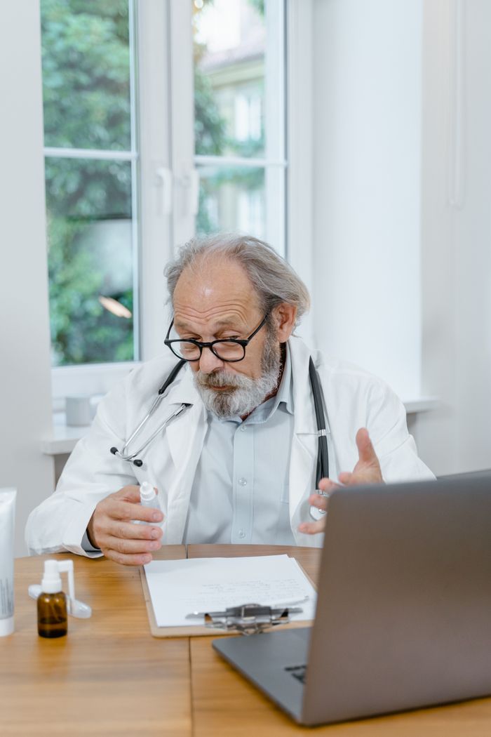 Elderly doctor explaining medication during an online consultation in a well-lit office setting.
